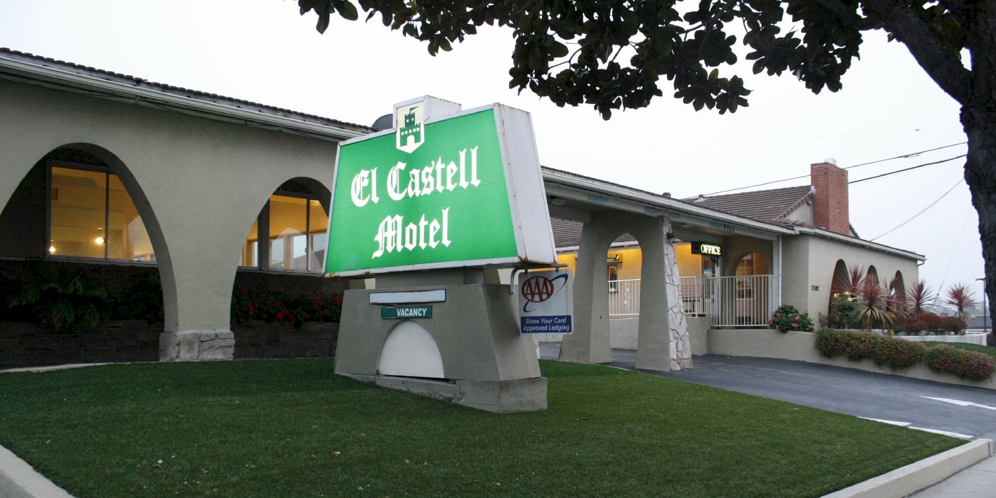 A retro-style motel with a bright green “El Castell Motel” sign on a raised grassy island in front of a low, arched building.