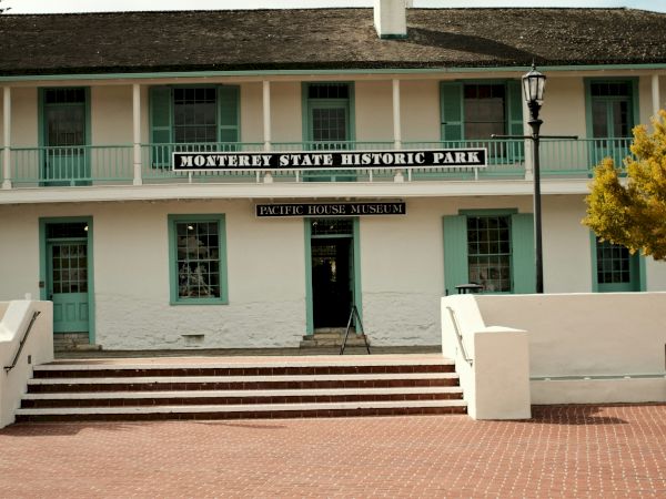 A two-story white building with green railings and a sign reading “Granary School History Club,” red brick steps, and a wide brick plaza in front.