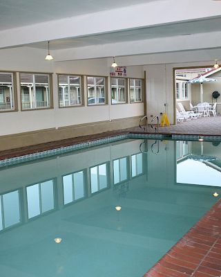 Indoor swimming pool area with clear water, tiled deck, windows along one wall, and a lounge/locker room visible in the background.